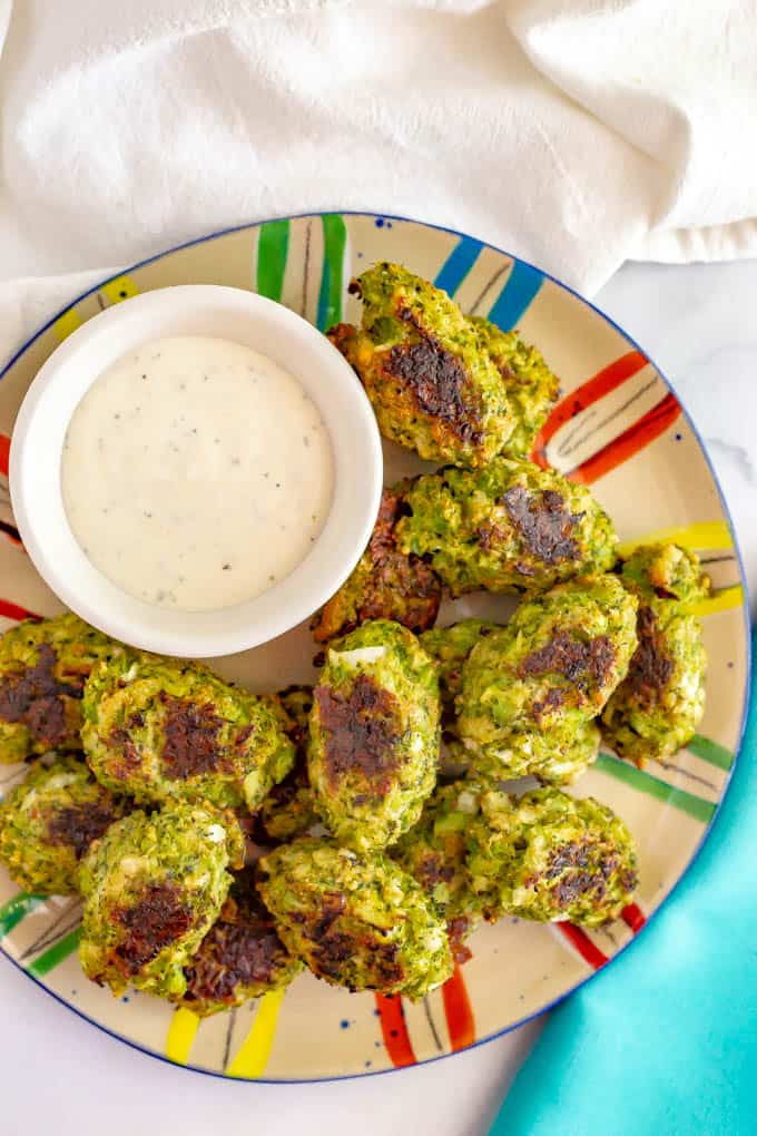 Baked broccoli tots piled on a colorful plate with a bowl of Ranch dressing for a dip