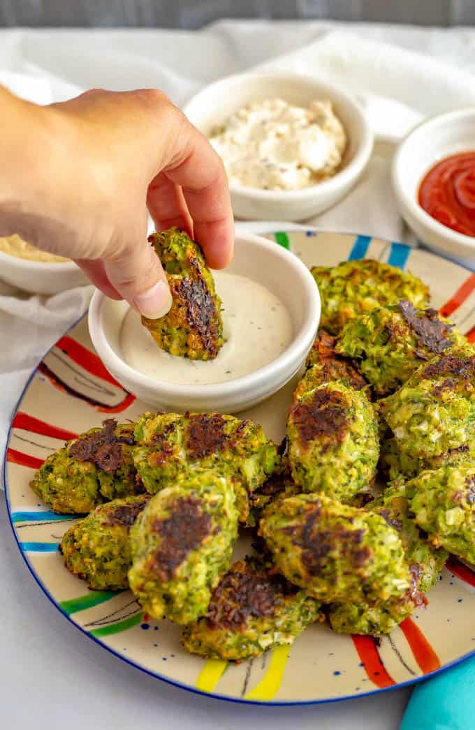 These easy baked broccoli tots are just 5 ingredients and make a great healthy veggie side dish or finger food for kids to serve with Ranch, ketchup or honey mustard for dipping! #broccoli #kids #healthyrecipe A hand dipping a broccoli tot into a small bowl of Ranch dressing.