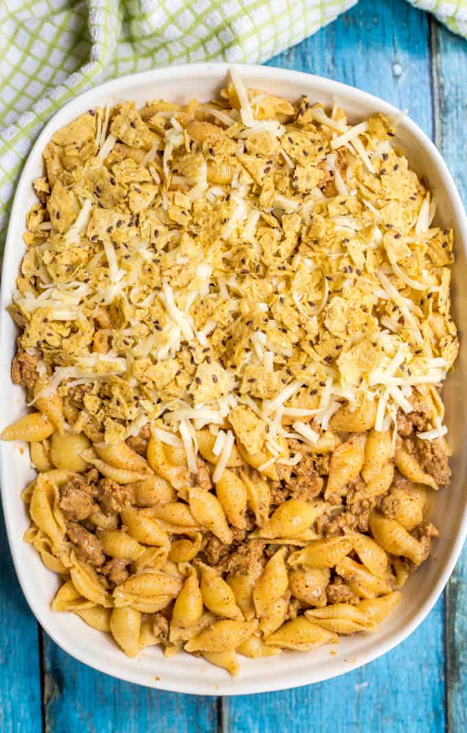 Baked taco mac and cheese casserole being assembled with a tortilla chip and cheese topping