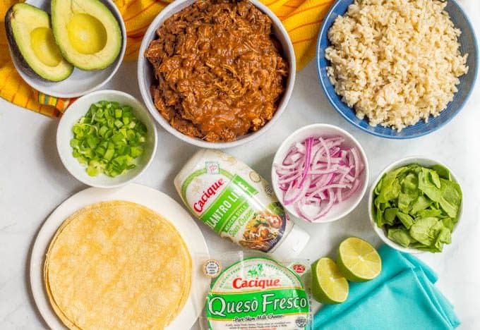 Ingredients for easy crock pot mole chicken laid out in different bowls on a white marble countertop