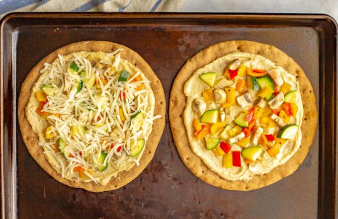 Hummus pita pizzas with veggies and cheese on a baking tray before being baked