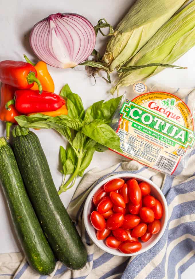 Ingredients for summer veggie skillet laid out on a marble table with a blue towel