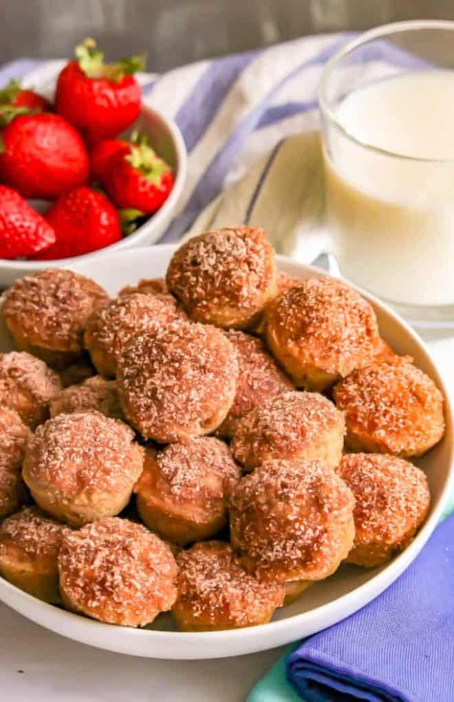 Apple cinnamon donut holes in a large white bowl with strawberries and a glass of milk in the background.