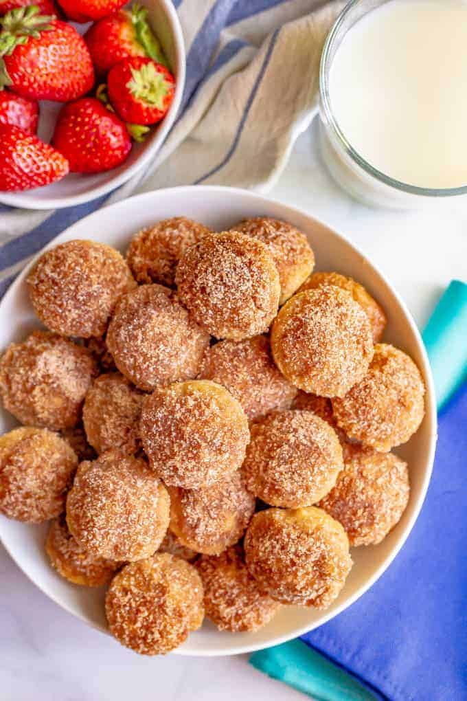 Homemade baked donut holes in a large white bowl with strawberries and milk to the side.