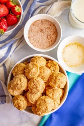 Baked apple cinnamon donut holes piled up in a large bowl and bowls for dunking in a butter and cinnamon sugar coating