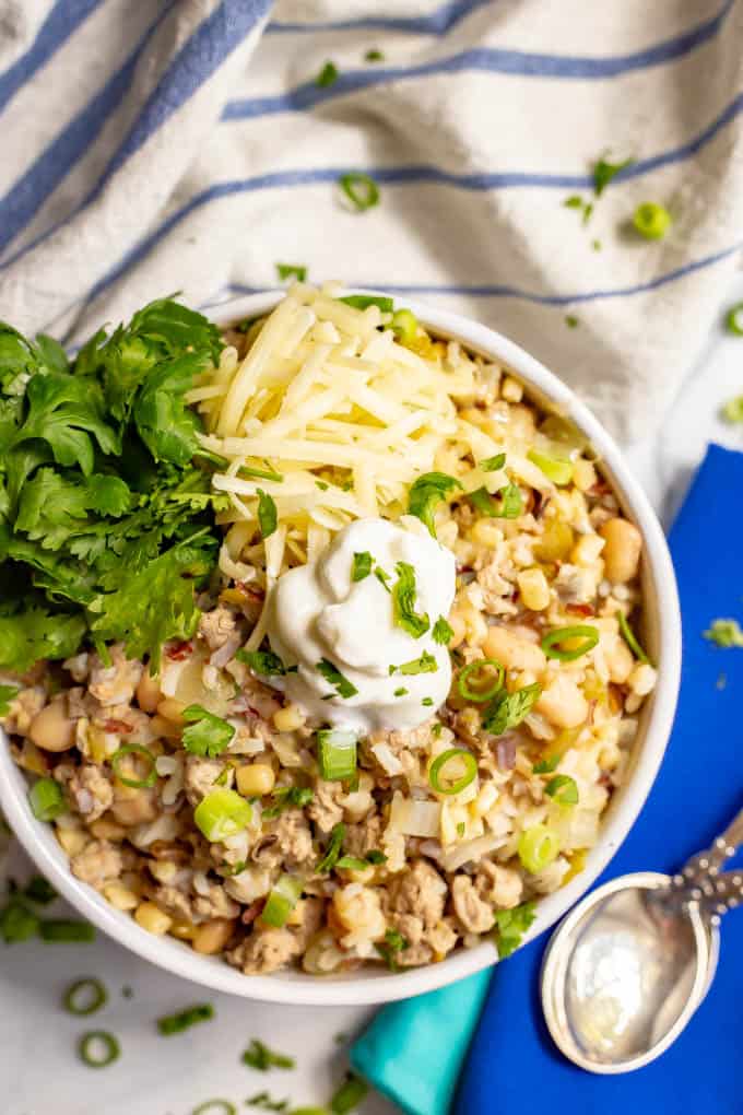This easy, healthy white turkey chili comes together in about 30 minutes with some simple pantry ingredients. It's full of hearty ground turkey pieces, white beans, rice, corn and green chilies for a hearty meal! #turkeychili #chili #easyrecipe #groundturkey A bowl of white turkey chili topped with sour cream, cilantro and shredded cheese with two spoons to the side.