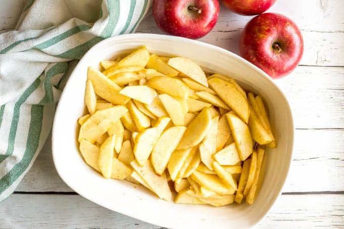 Sliced apples in a large white casserole dish before being covered with a cobbler topping