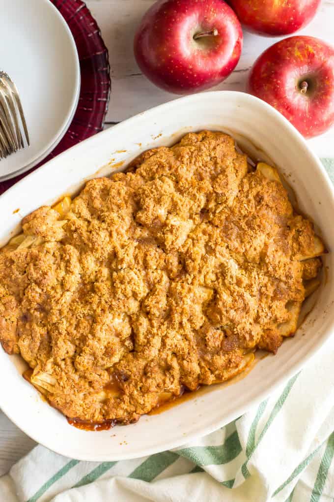 Healthy apple cobbler in a white casserole dish with red apples nearby