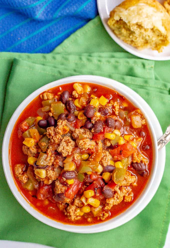 A bowl full of healthy southwest turkey chili with corn and black beans on a green napkin with cornbread on a separate plate