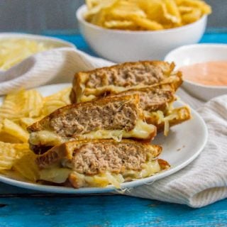 Ground turkey patty melt sandwich sliced and stacked on a white plate with chips on the side