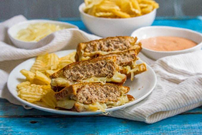 Ground turkey patty melt sandwich sliced and stacked on a white plate with chips on the side