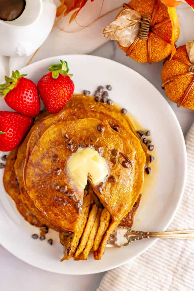 A stack of whole wheat pumpkin pancakes on a white plate with butter and mini chocolate chips on top