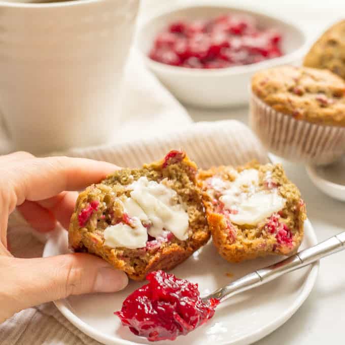 Whole wheat cranberry sauce muffin served on a plate with butter on top and being picked up