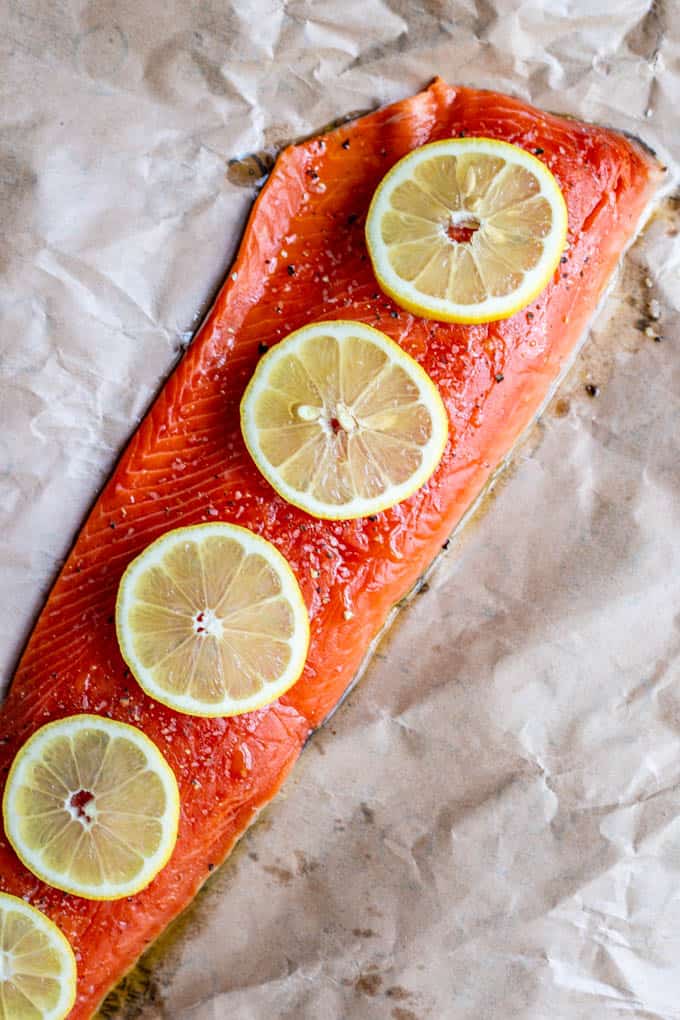 Raw wild-caught salmon on a pice of parchment paper with lemon slices on top