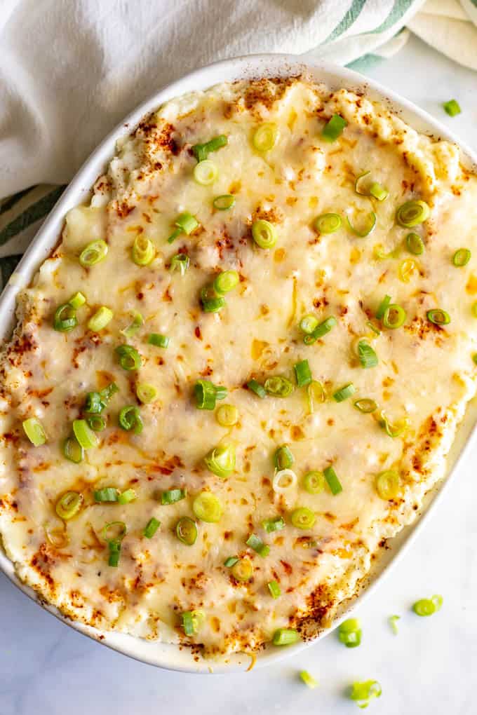 Baked mashed cauliflower casserole with green onions sprinkled on top, in a large white casserole dish