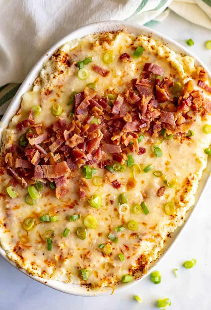 Mashed cauliflower casserole with cheese, bacon and green onions on top, in a large white casserole dish