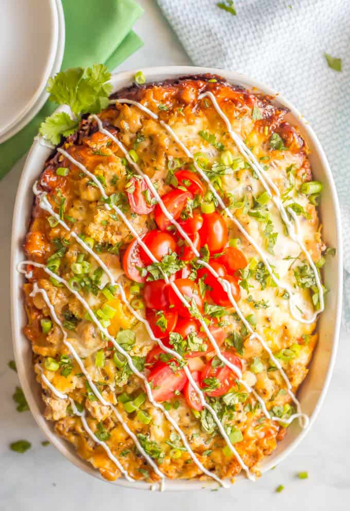 Overnight slow cooker breakfast casserole in a white baking dish with tomatoes and green onions and cilantro sprinkled on top