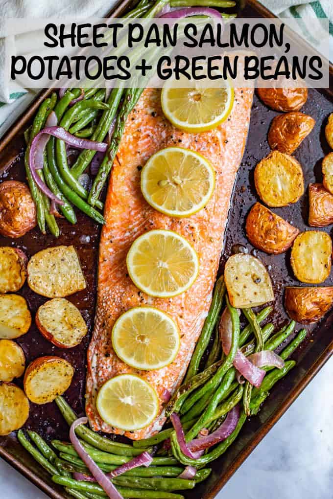 A sheet pan with a long piece of roasted salmon topped with lemon slices alongside roasted potatoes and green beans.