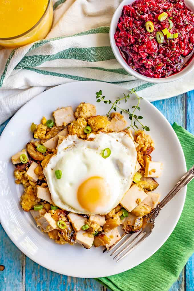 Leftover Thanksgiving turkey and sides in a breakfast hash served on a white plate with a fried egg on top