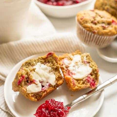 Whole wheat cranberry sauce muffin split in half, smeared with butter and served on a small white plate