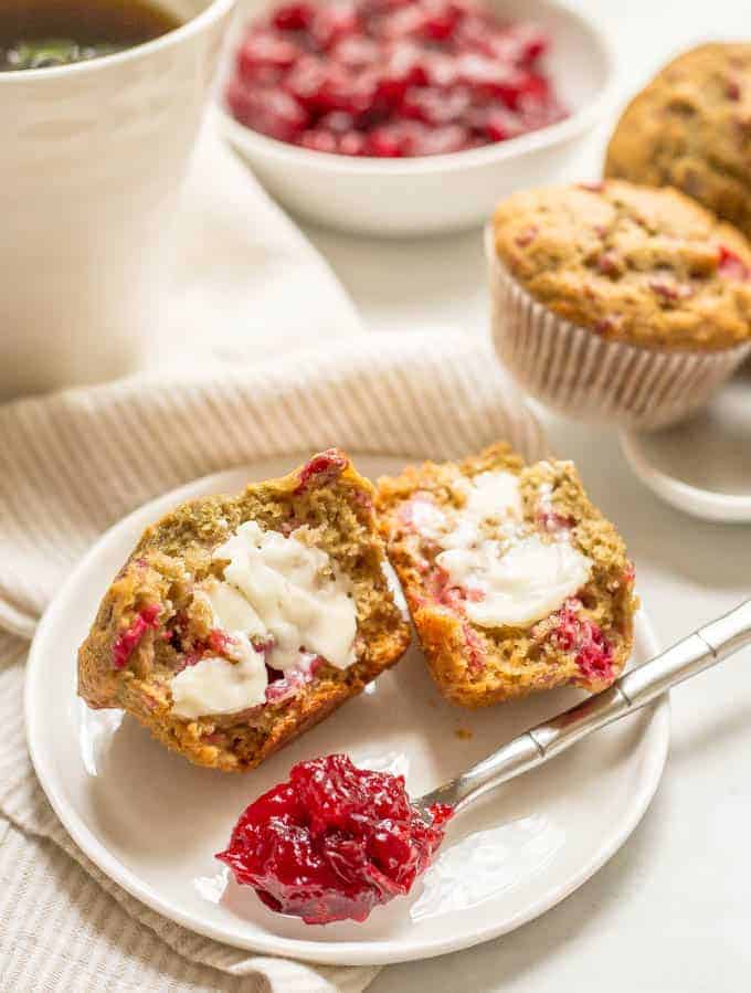 Whole wheat cranberry sauce muffin split in half, smeared with butter and served on a small white plate