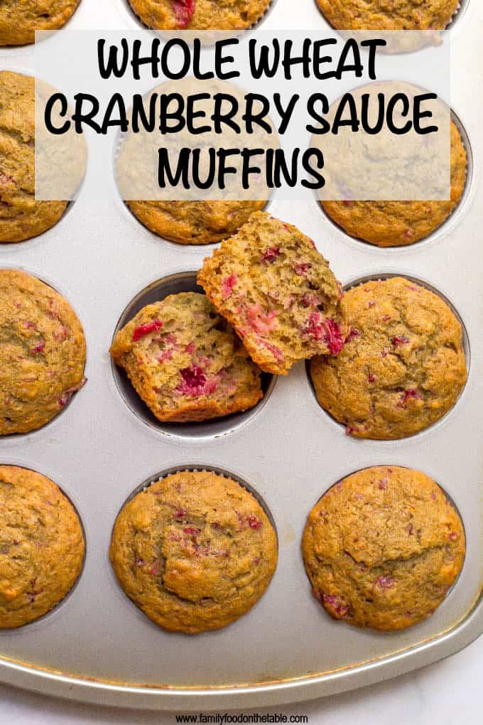 A muffin tin full of baked cranberry sauce muffins with one split open to show the insides.