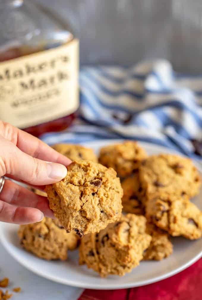 Bourbon chocolate chip cookies on a white plate with someone holding one up