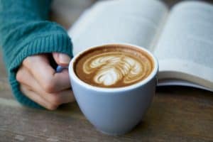 Coffee latte in a mug with a hand on handle and a book in the background