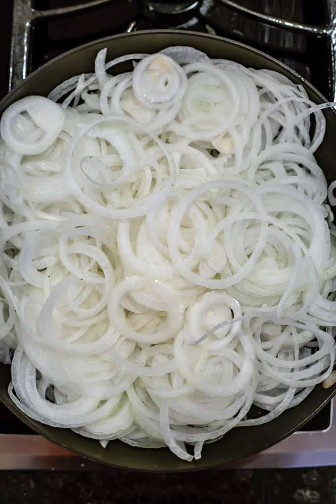 Large heap of sliced onions in a pan before being cooked down