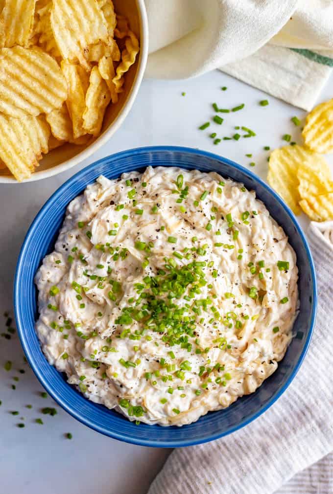 Healthier caramelized onion dip served in a blue bowl with chives on top and chips nearby for dipping
