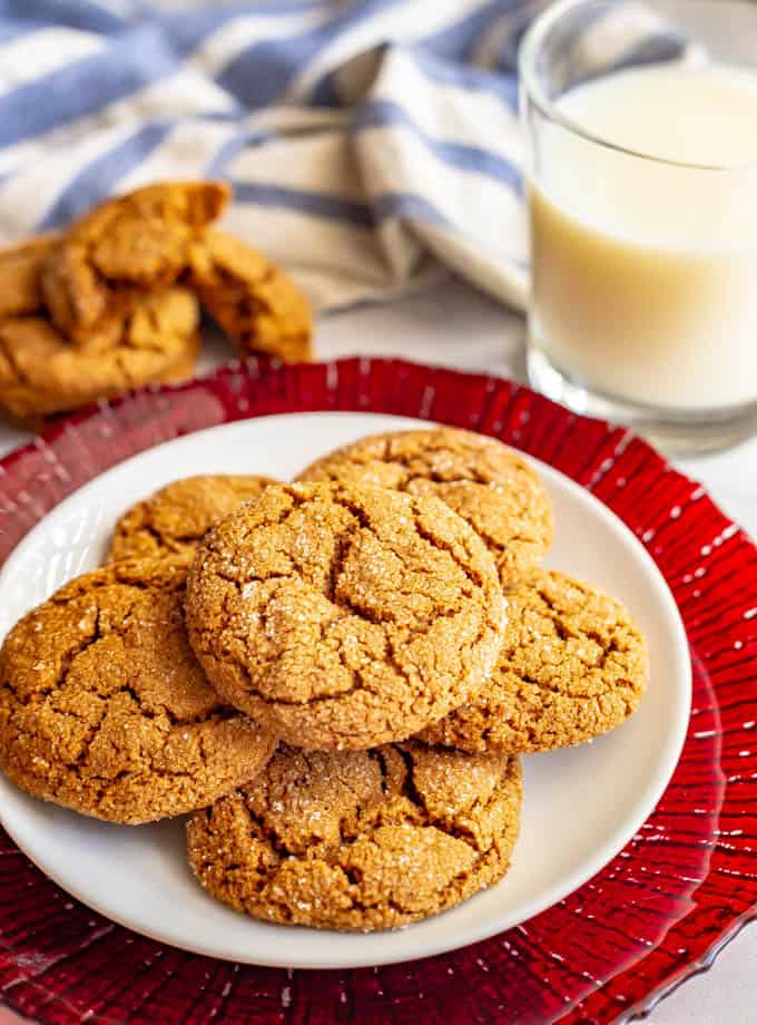 Old fashioned molasses cookies piled on a white plate with a glass of milk in the background.