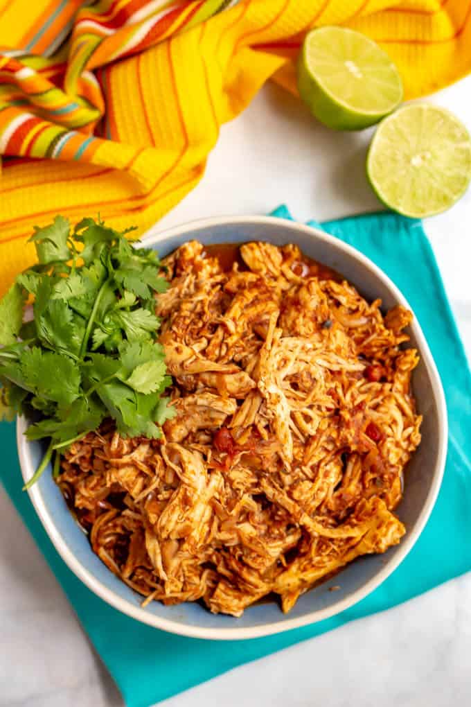 A bowl of crock pot Mexican shredded chicken with cilantro on the side and a cut lime on the table