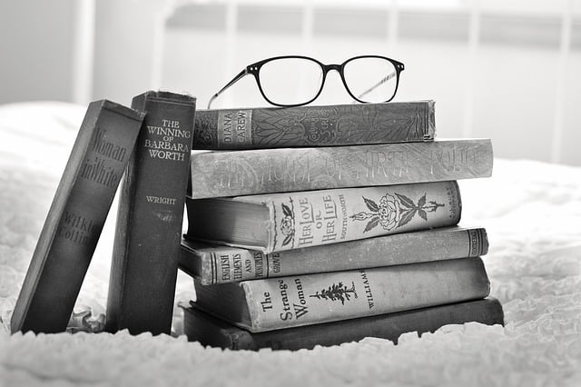 Black and white photo of a stack of books with glasses perched on top