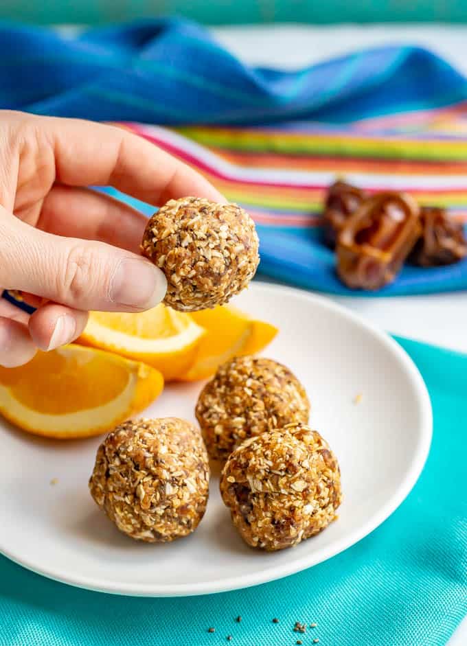 Healthy peanut butter energy balls on a white plate with sliced oranges and one being held up