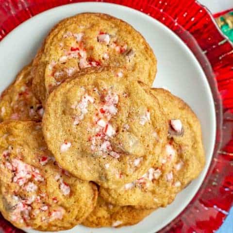 Peppermint chocolate chip cookies piled on a white plate with a red plate underneath and candy canes to the side