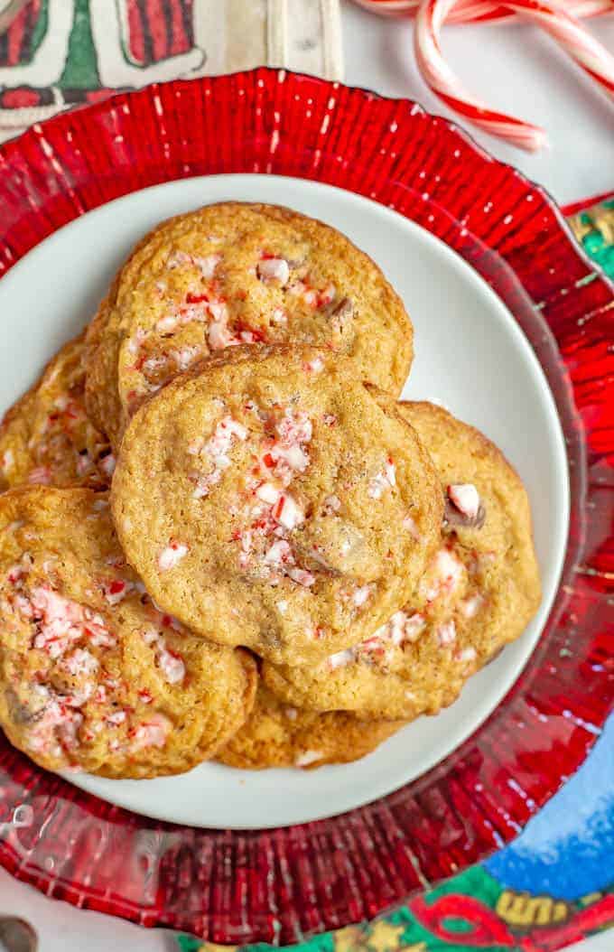 Peppermint chocolate chip cookies piled on a white plate with a red plate underneath and candy canes to the side