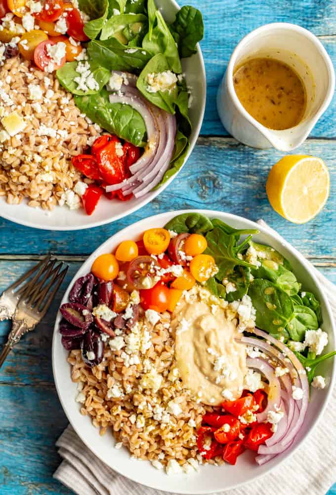 Loaded Greek grain bowls with farro, hummus, tomatoes, spinach, peppers, olives, red onion and feta cheese