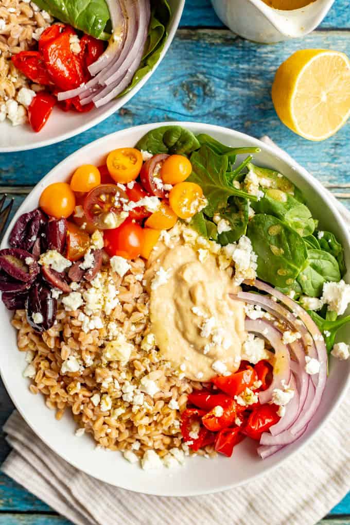 A grain bowl with farro, tomatoes, spinach, red onions and peppers in separate piles with hummus in the middle and feta cheese sprinkled over top of everything.
