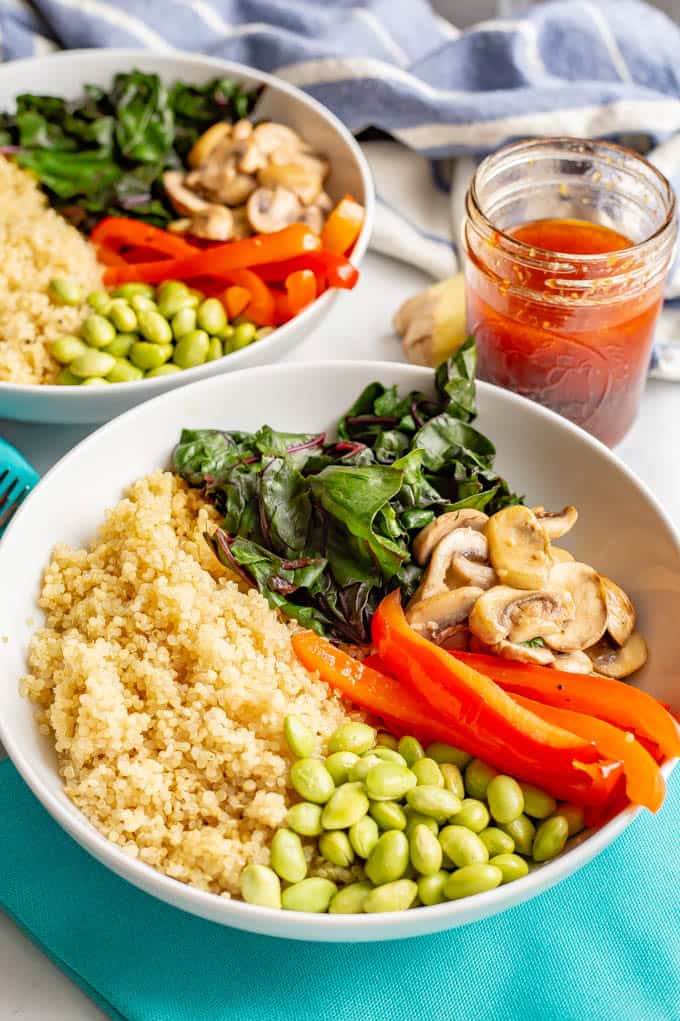 Asian quinoa power bowls with greens, mushrooms, peppers and edamame with napkins and soy ginger dressing laid out