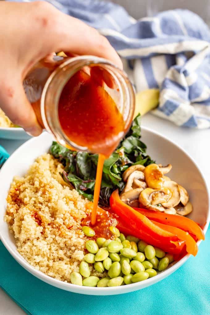 Soy ginger dressing being poured over an Asian style quinoa bowl with veggies