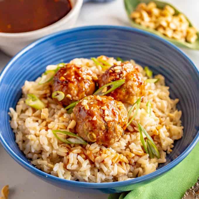 Baked Asian turkey meatballs served on a bed of brown rice with green onions and peanuts sprinkled on top