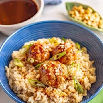 Turkey meatballs on top of steamed brown rice in a blue bowl with a hoisin sauce drizzled on top.