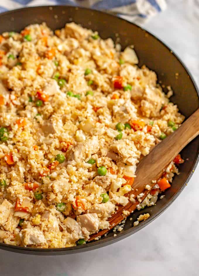 Cooked cauliflower fried rice with chicken in a skillet with a wooden spoon