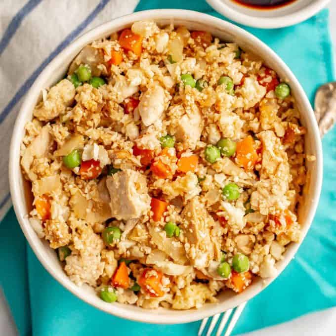 Cauliflower fried rice with chicken, peas and carrots in a white bowl on a turquoise napkin