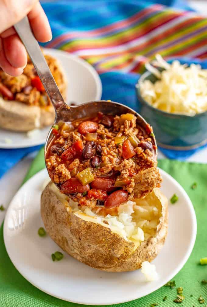Chili being ladled onto a fluffy baked potato