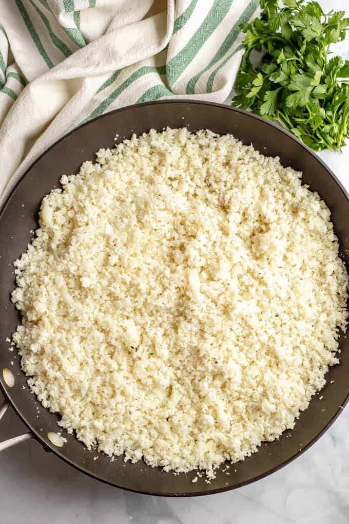 Cauliflower that's been broken down into small pieces being cooked in a large skillet