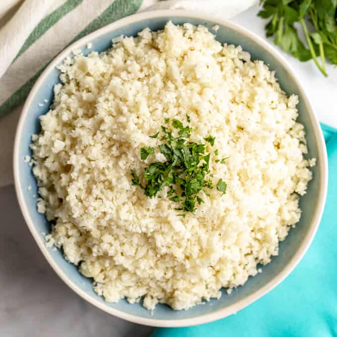 Cooked riced cauliflower in a round blue bowl with a sprinkling of chopped parsley