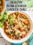 A chicken chili with beans and tomatoes served in a white bowl with shredded cheese on top.