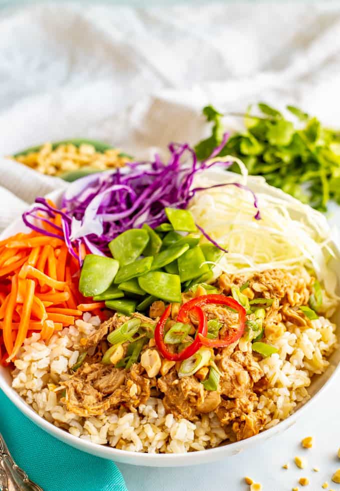 A large white bowl with rice, peanut chicken, cabbage, carrots and snow peas