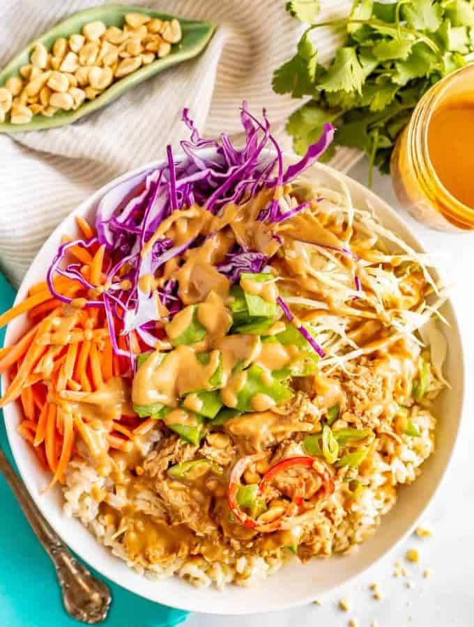 A rice bowl with shredded cabbage, carrots and peanut chicken all drizzled with a peanut dressing and sprinkled with sliced green onions.